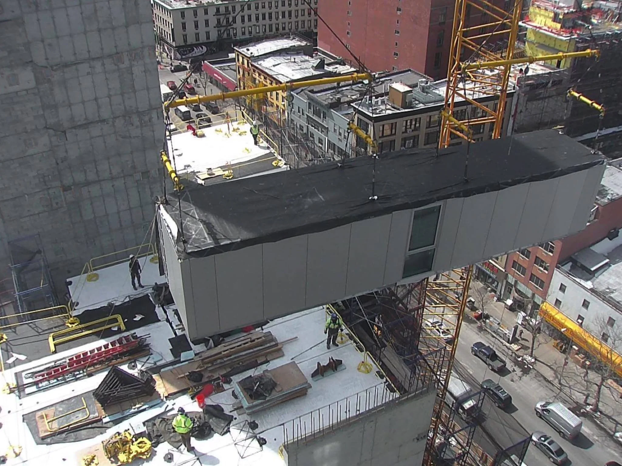 A finished modular unit being lifted by crane into a high-rise under construction in New York City